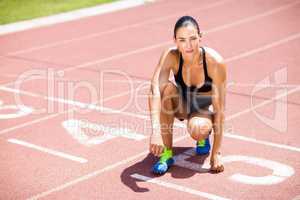 Portrait of female athlete kneeling on running track