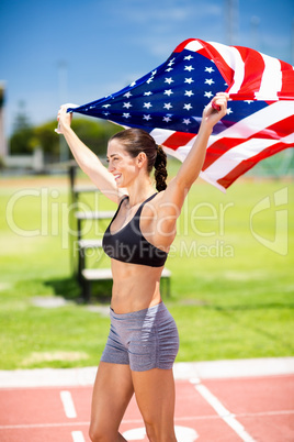 Happy female athlete holding up american flag on running track