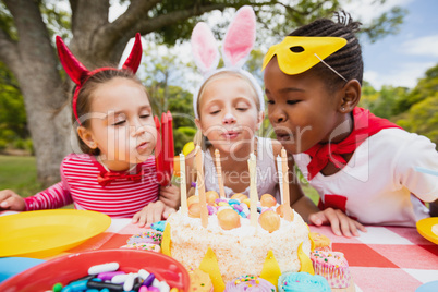 Three little girls blowing together birthday candles