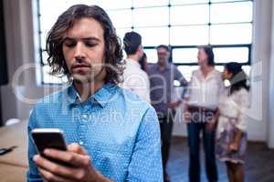 Hipster using a smartphone and group of coworkers