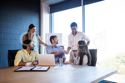 Group of coworkers interacting around a table and handshaking