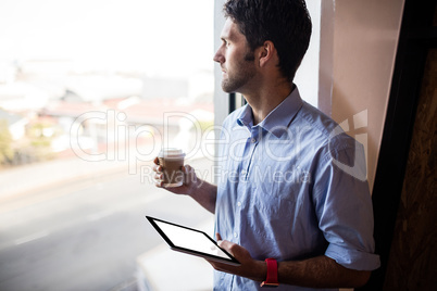 Casual businessman holding a cup of tea and a tablet computer
