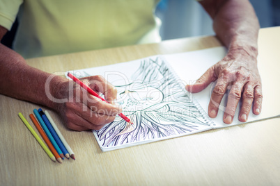 Senior man drawing with a colored pencil in drawing book