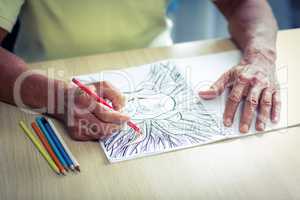 Senior man drawing with a colored pencil in drawing book