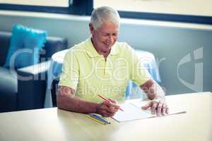 Senior man drawing with a colored pencil in drawing book