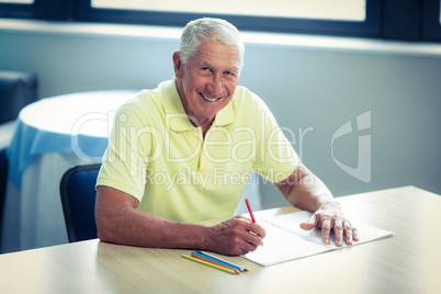 Senior man drawing with a colored pencil in drawing book