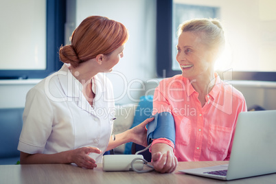 Female nurse checking blood pressure of senior woman