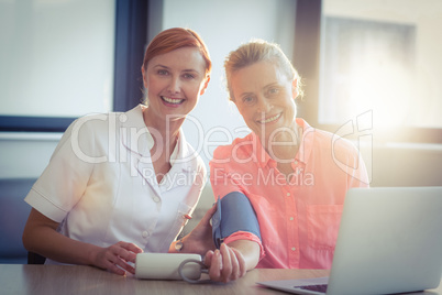 Female nurse checking blood pressure of senior woman