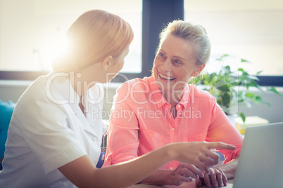 Female nurse and senior woman smiling while using laptop