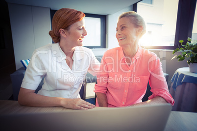 Female nurse and senior woman smiling while using laptop