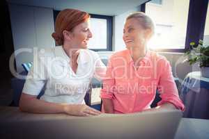 Female nurse and senior woman smiling while using laptop