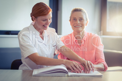 Female nurse helping patient in reading the braille book