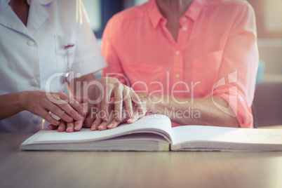 Female nurse helping patient reading the braille book