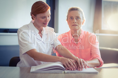 Female nurse helping patient in reading the braille book