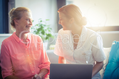 Female nurse and senior woman smiling while using laptop