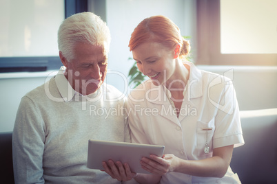 Female nurse showing medical report to senior man on digital tablet