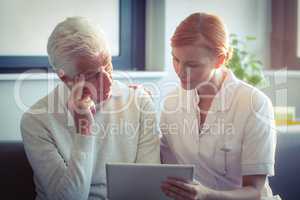 Female nurse showing medical report to senior man on digital tablet