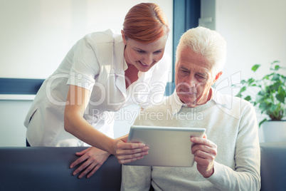 Female nurse showing medical report to senior man on digital tablet