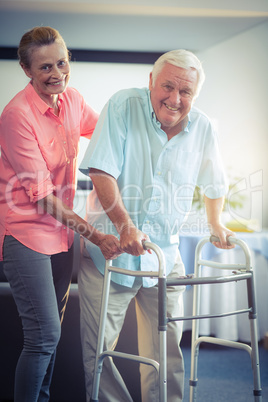 Senior woman helping senior man to walk with walker
