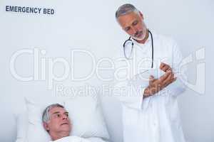 Male doctor writing medical report of senior man on clipboard