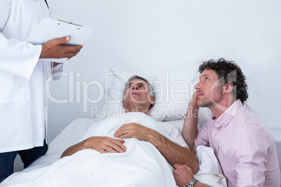 Man sitting next to patients bed and listening to the doctor