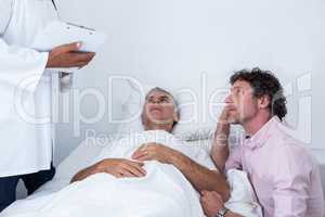 Man sitting next to patients bed and listening to the doctor