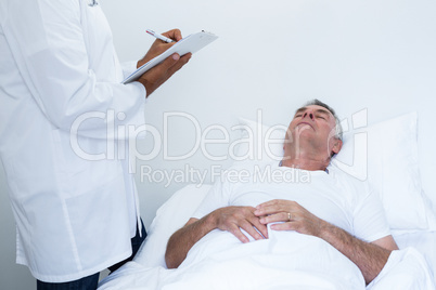 Male doctor writing medical report of senior man on clipboard