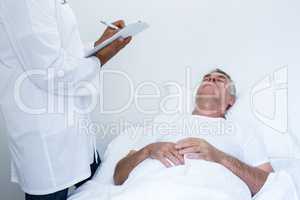 Male doctor writing medical report of senior man on clipboard