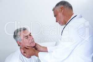 Male doctor examining senior mans neck