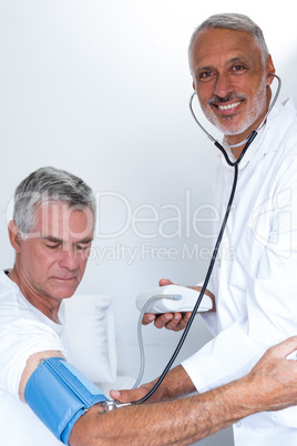 Male doctor checking senior mans blood pressure