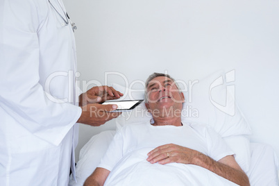 Male doctor standing next to the patient and holding a digital tablet
