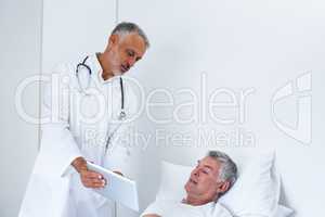 Male doctor discussing medical reports with senior man on digital tablet