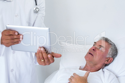Male doctor discussing medical reports with senior man on digital tablet