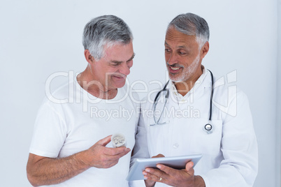 Male doctor showing medical reports to senior man on digital tablet