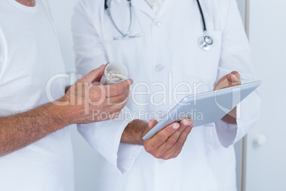 Male doctor showing medical reports to senior man on digital tablet