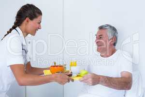 Female doctor serving breakfast to senior man