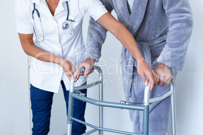 Mid-section of female doctor helping senior man to walk with walker