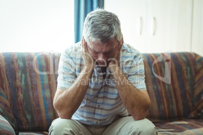 Upset senior man sitting in living room