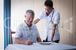 Doctor assisting a senior man while drawing in drawing book