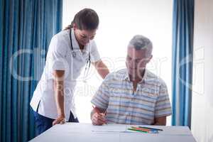 Doctor assisting a senior man while drawing in drawing book