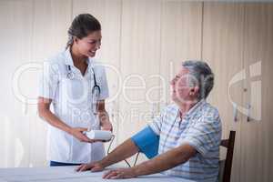 Female doctor checking blood pressure of senior man