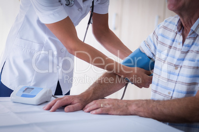 Mid-section of female doctor checking blood pressure of senior man