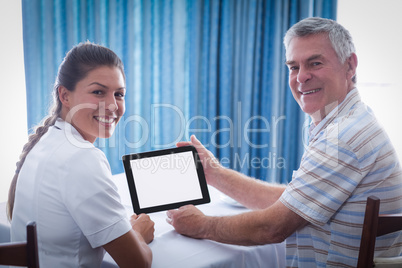 Portrait of senior man and female doctor using digital tablet