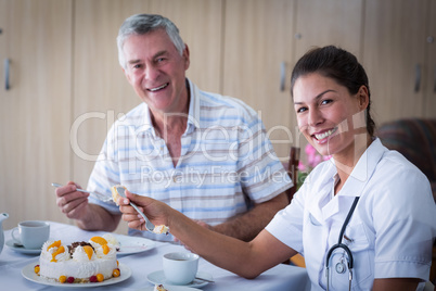 Senior man and female doctor talking while having cake in living room