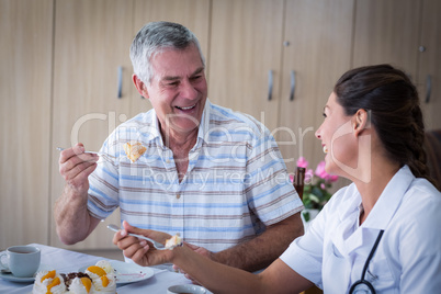 Portrait of senior man and female doctor having cake in living room