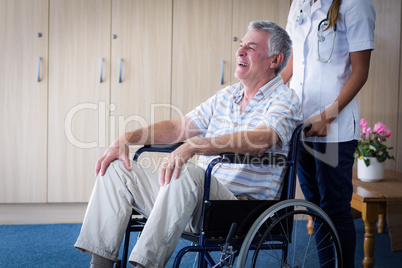 Female doctor carrying senior man on wheelchair