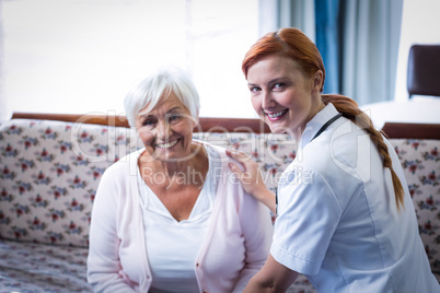 Portrait of smiling senior woman and female doctor in living room