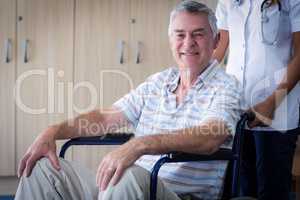 Female doctor carrying senior man on wheelchair