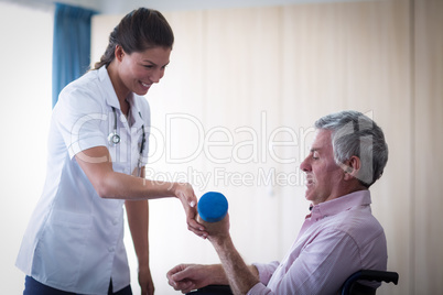 Female doctor assisting senior man in lifting dumbbell