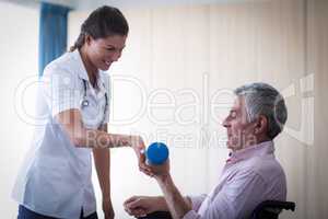 Female doctor assisting senior man in lifting dumbbell